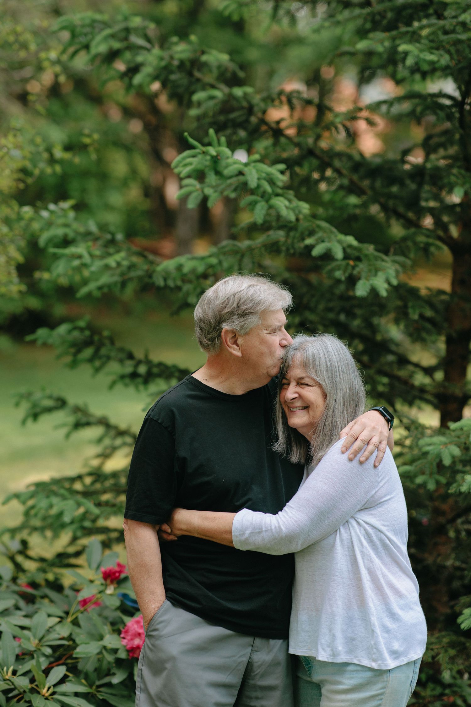 A loving senior couple embraces and shares a joyful moment together among green foliage in an outdoor setting.