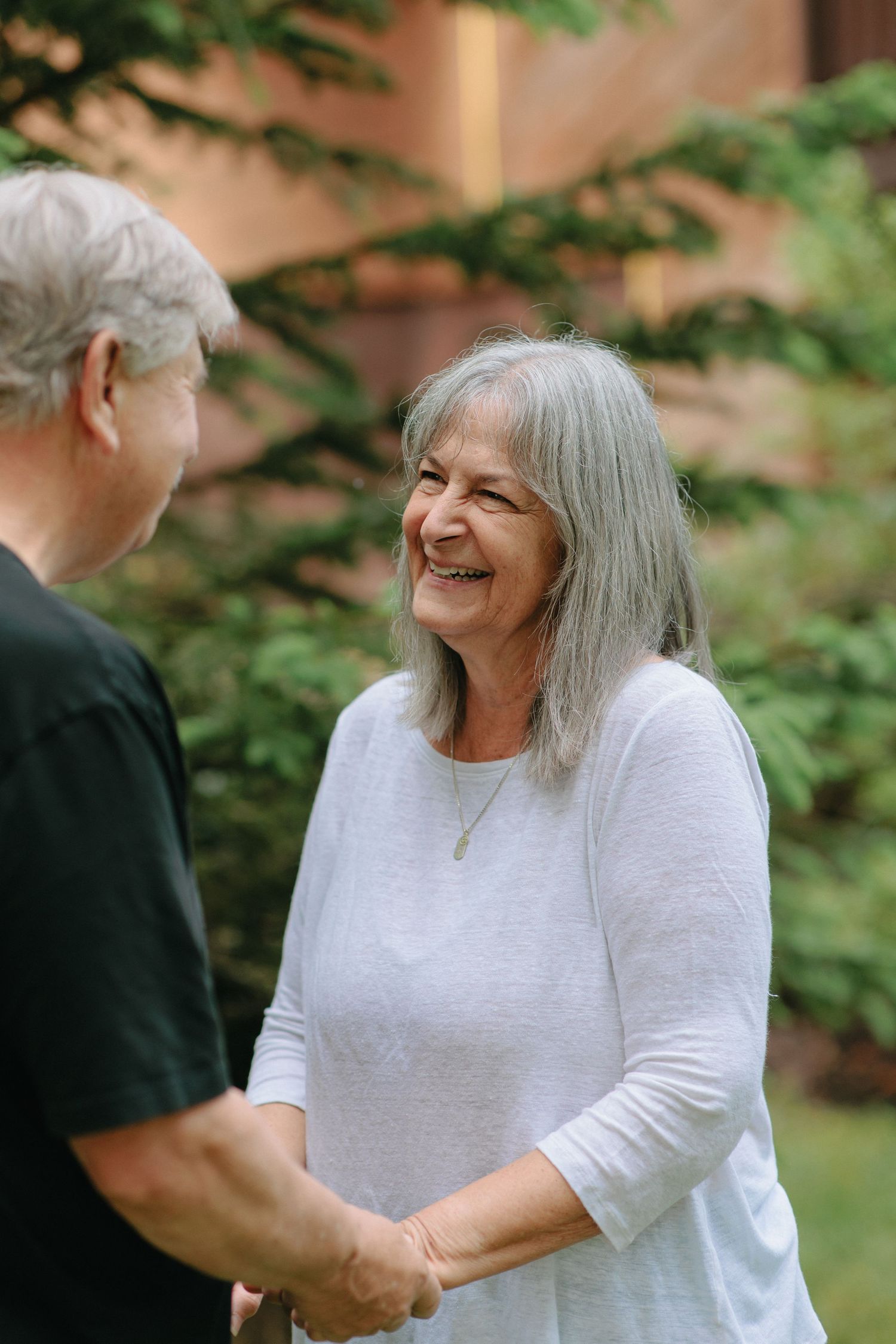 Two seniors sharing a joyful laugh while holding hands in an outdoor garden setting.