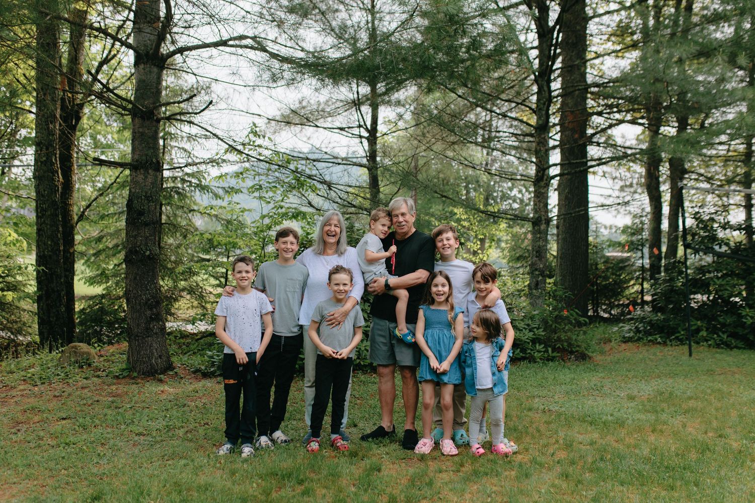 A group poses together for a family photo outdoors in a serene forest setting with tall pine trees in the background.