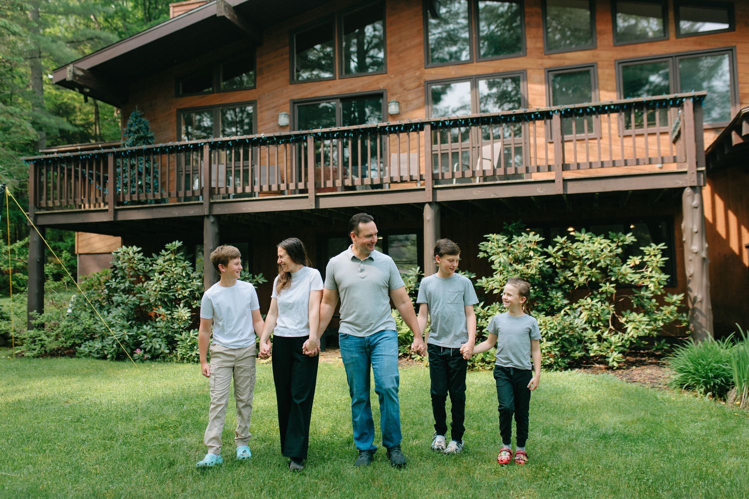 A group of friends walking through a grassy outdoor area near a rustic wooden cabin with a wrap-around deck.