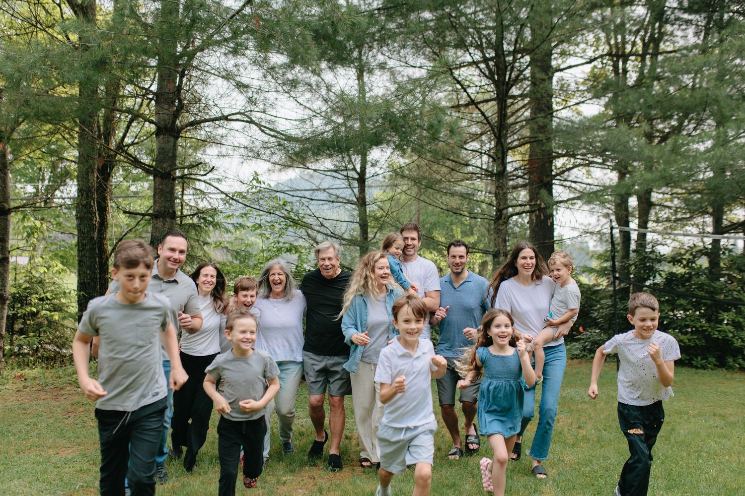 Family members run together playfully through a sunlit wooded area during an outdoor photo session.
