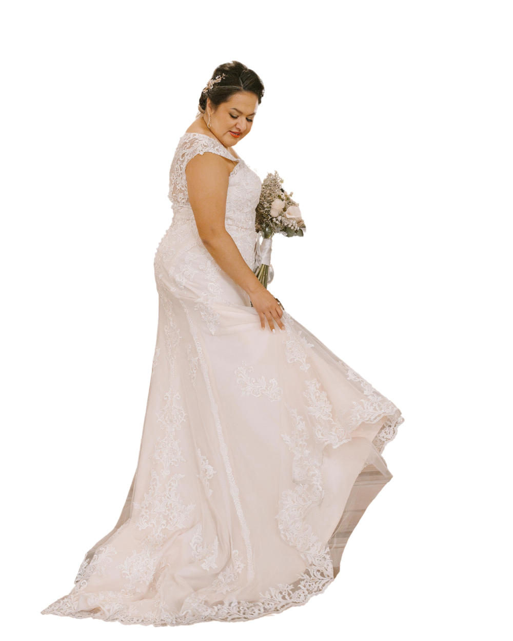Plus size bride in a white lace wedding dress with cap sleeves poses while holding up the skirt of her gown.