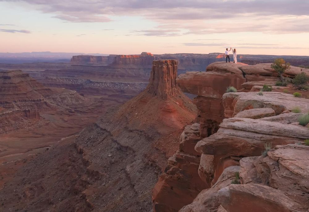 People standing on a red rock canyon cliff edge at sunset in Canyonlands National Park, Utah.