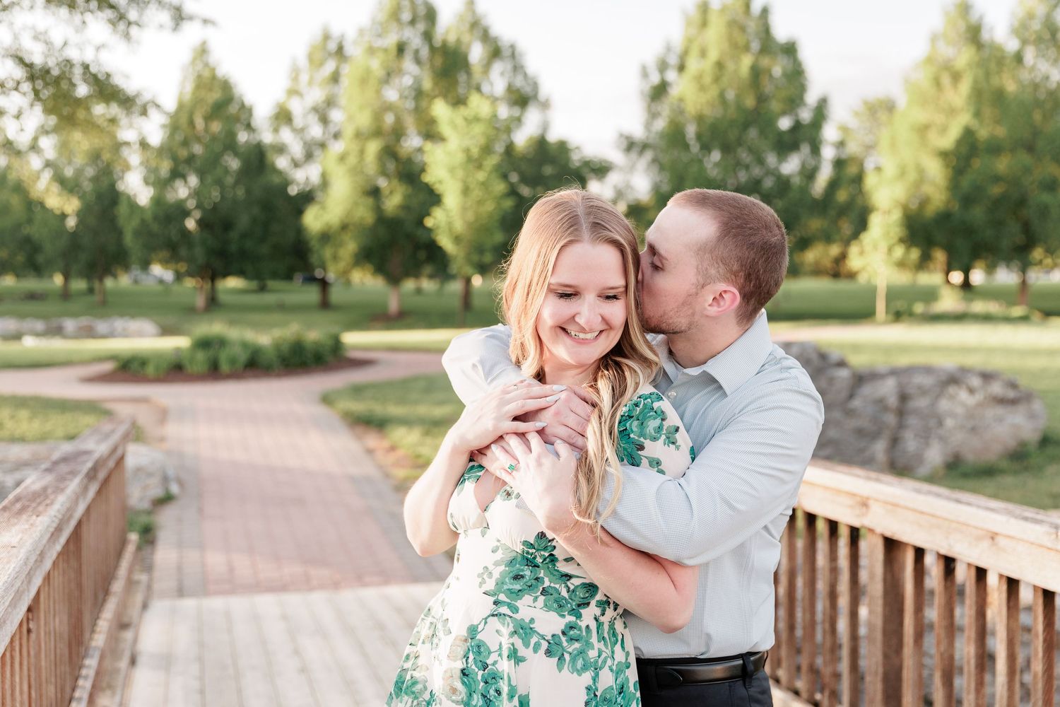 A couple shares an intimate embrace on a wooden bridge during a sunny winter day.