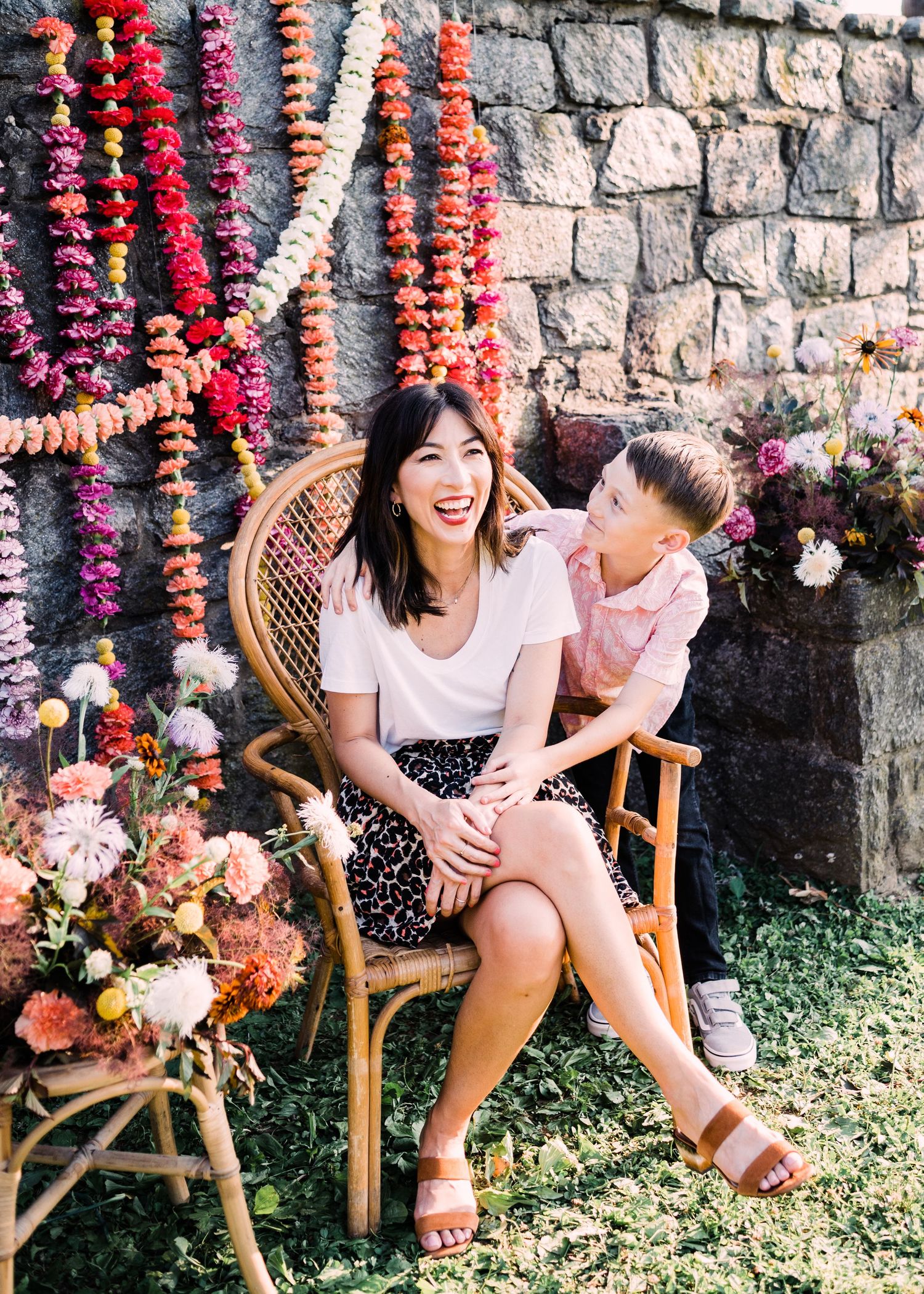 Beautiful outdoor scene with rattan peacock chair, colorful floral garlands, and stone wall backdrop, creating a joyful moment.