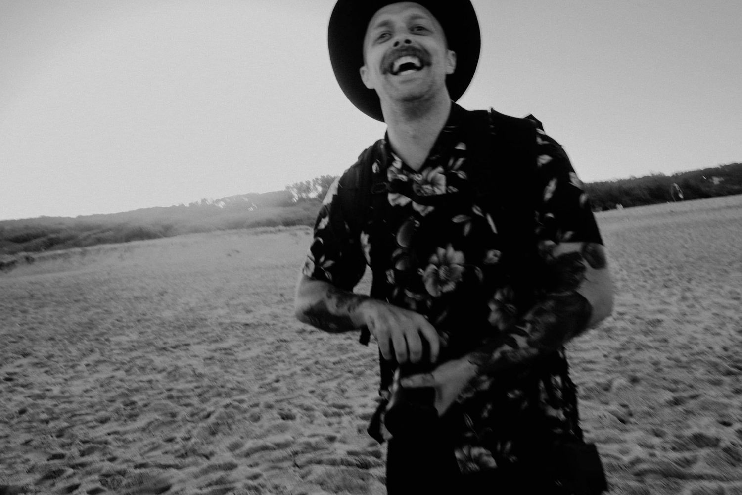 Child wearing a hat playing joyfully on a beach in black and white.