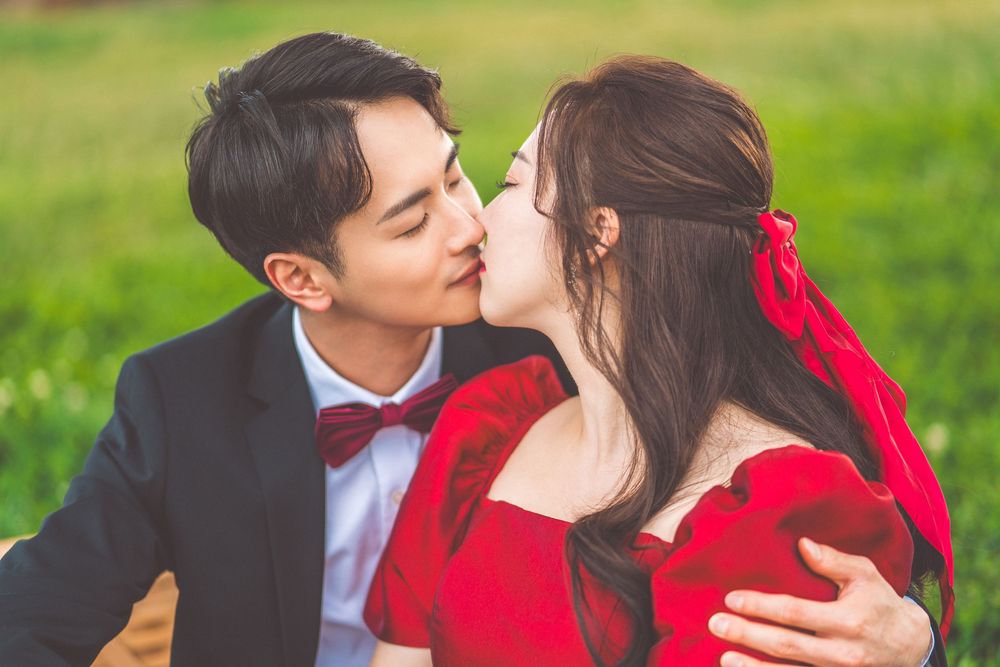 Intimate moment between a couple in formal attire sharing a tender kiss in a green field.