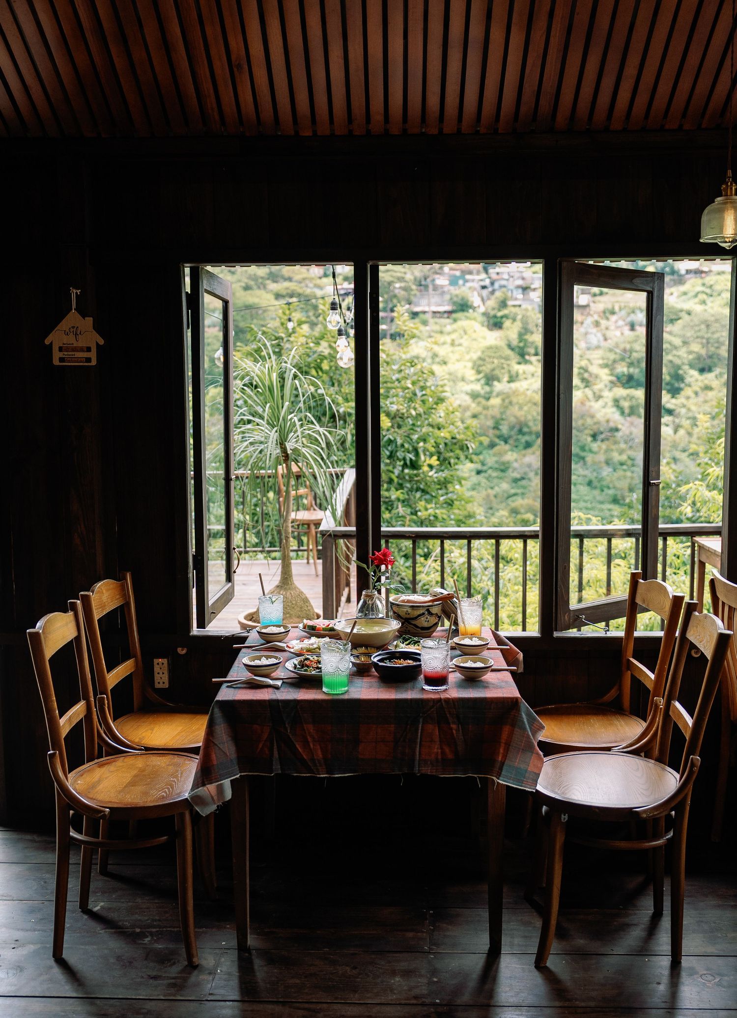 Rustic dining table set against panoramic mountain views through large windows in a cozy wooden interior.