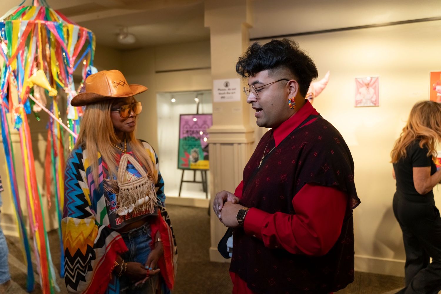 Two people in colorful outfits having a conversation in what appears to be a gallery or exhibition space.