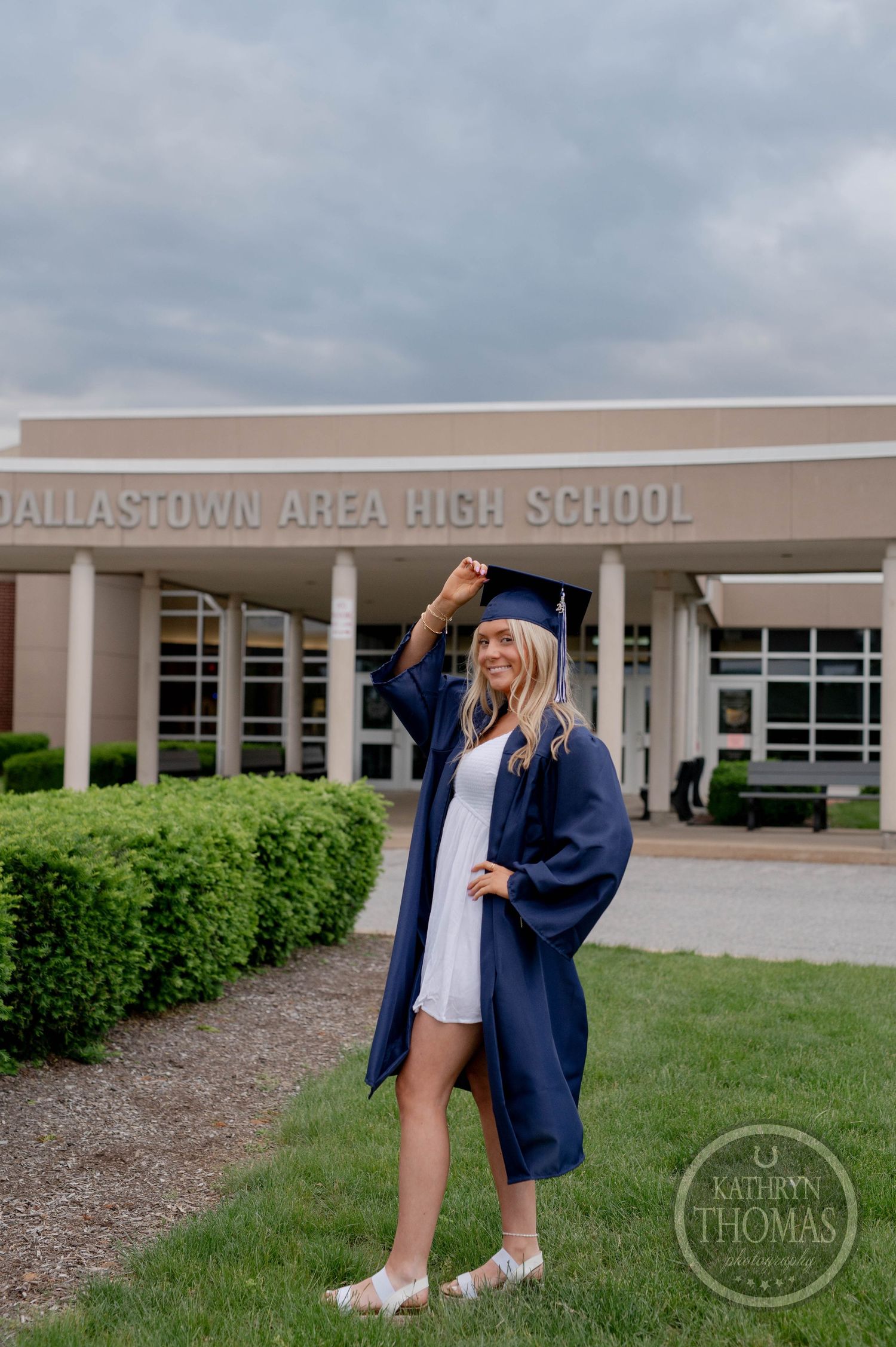 Graduate in navy blue cap and gown poses triumphantly outside Dallastown Area High School on graduation day.