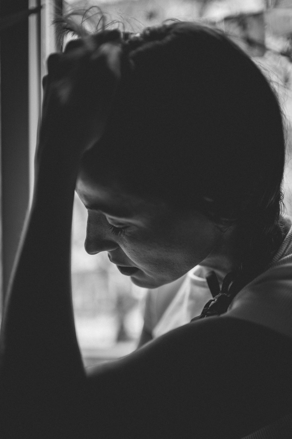 A black and white portrait photograph showing a person in profile view with downward gaze and dramatic side lighting.
