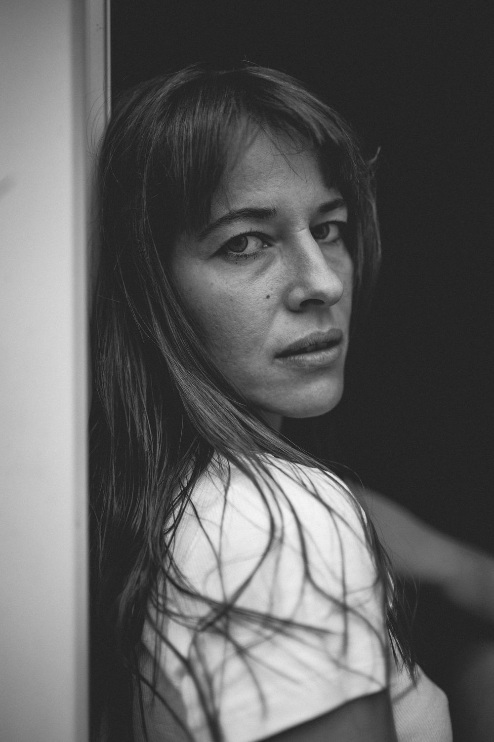 Black and white portrait photograph of a person with long hair gazing back over their shoulder in dramatic lighting.