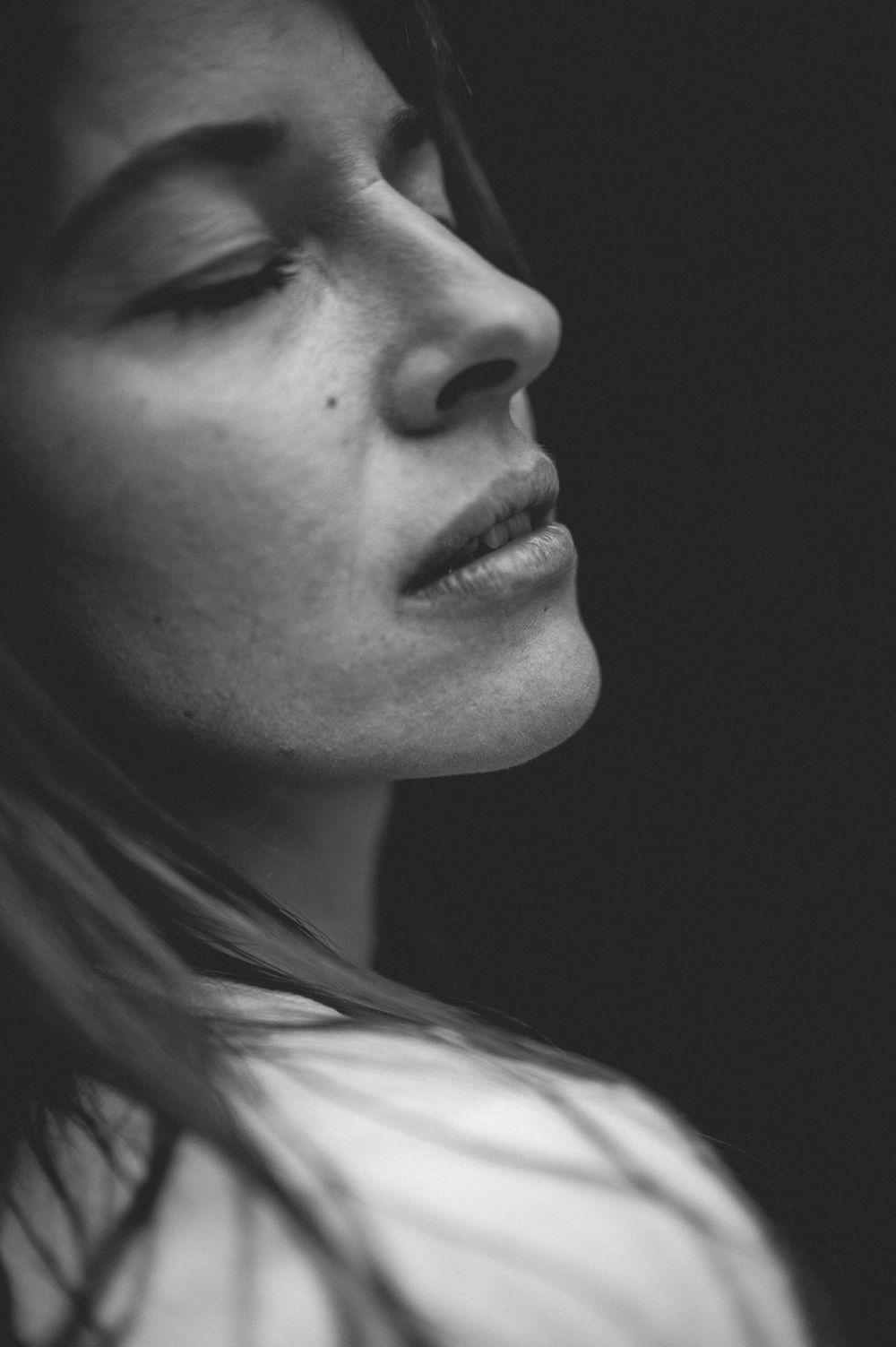 A black and white artistic portrait in profile showing serene expression with dramatic shadow and soft lighting.