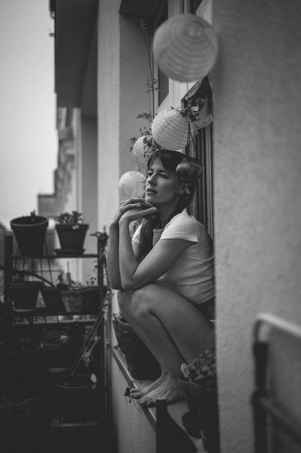 A person in casual attire sits by a window with a paper cup in a black and white artistic photograph series.