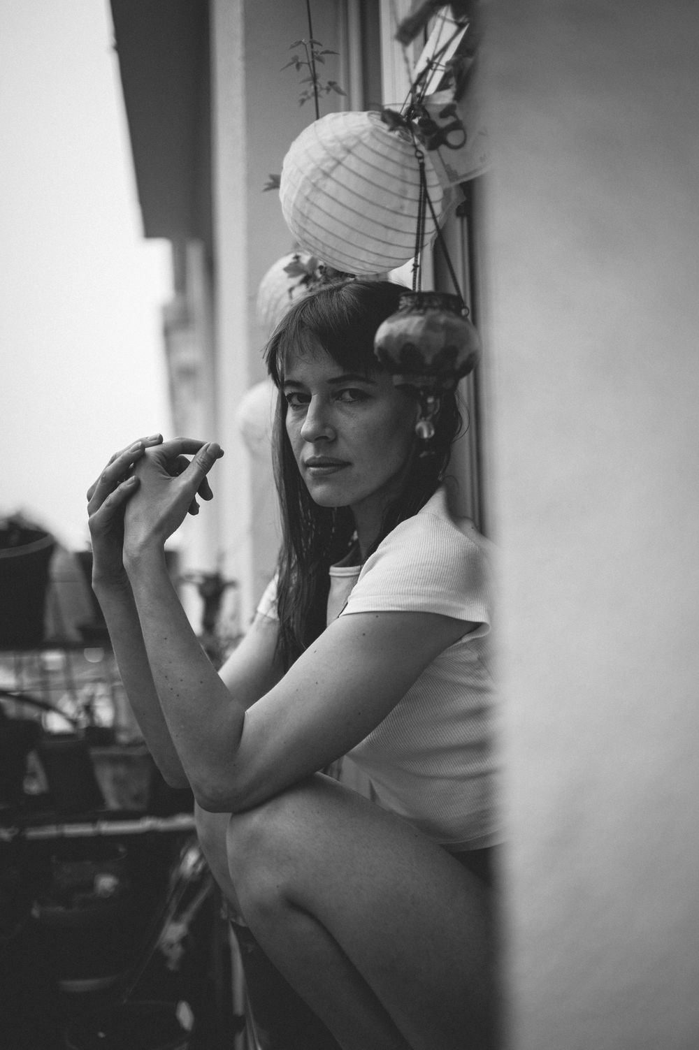 Black and white vintage photograph of a person in a white top leaning against a wall with a paper lantern decoration.