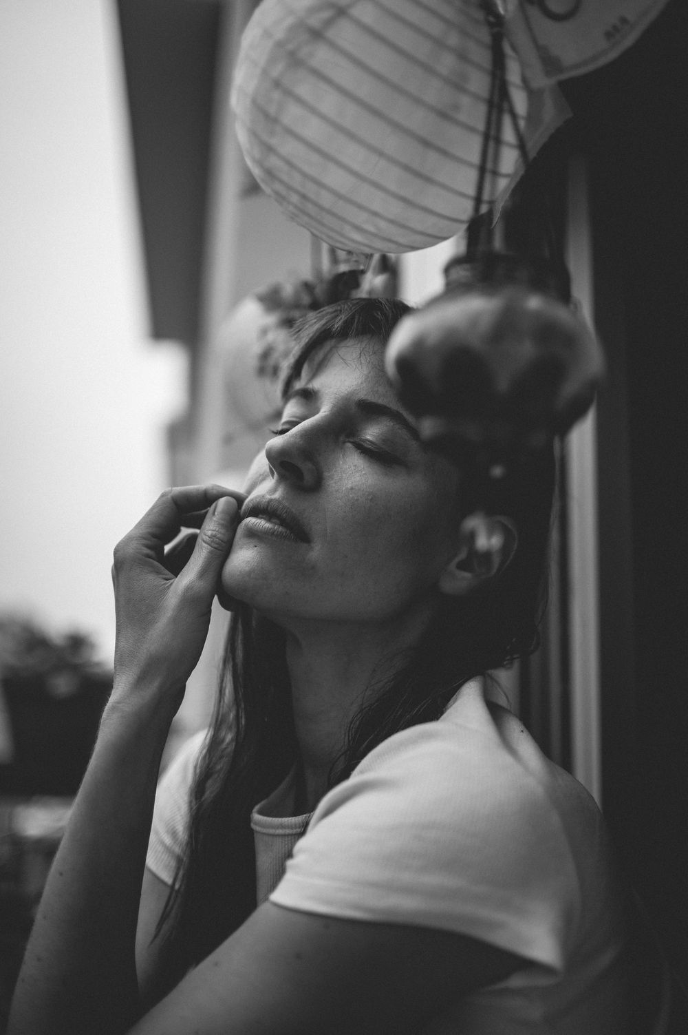 Artistic black and white portrait photo showing person smoking outdoors under paper lanterns with eyes closed.