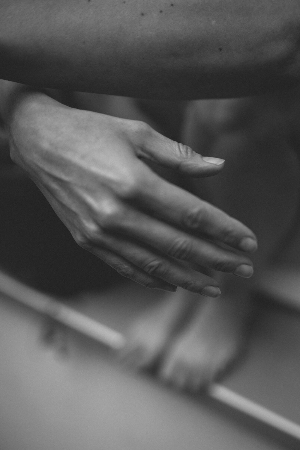 A graceful hand reaches outward in black and white, casting soft shadows against a dark background.