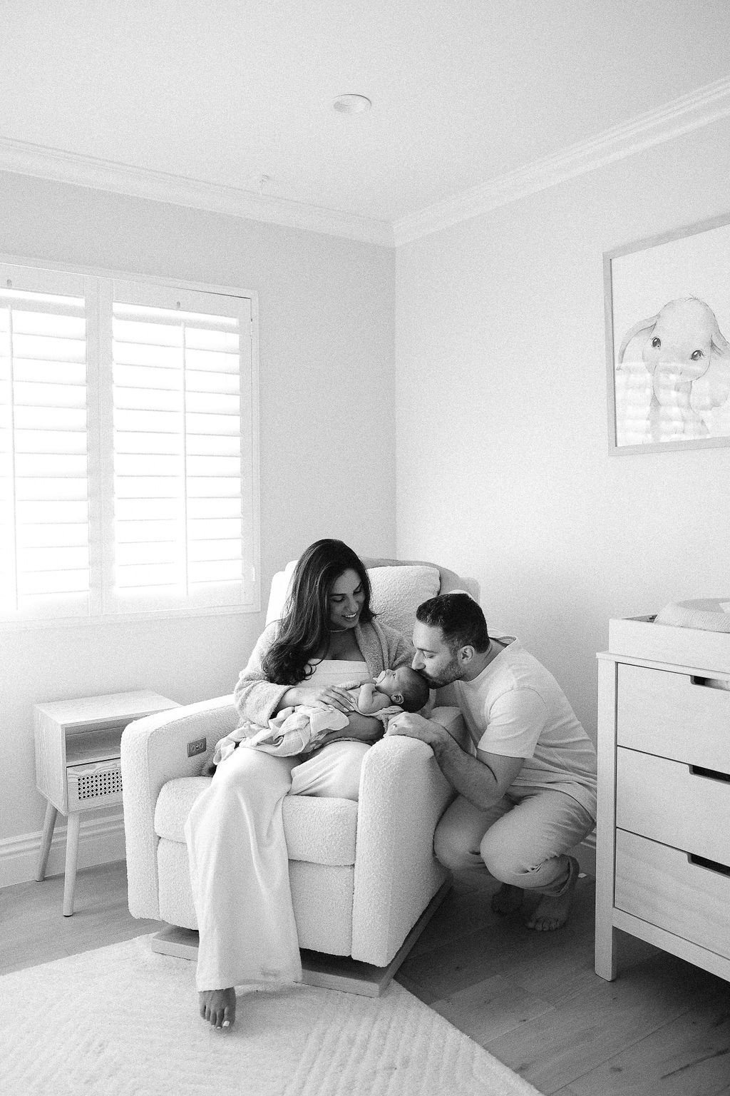 A tender family moment in a bright nursery as parents snuggle with their newborn baby in a cozy armchair.
