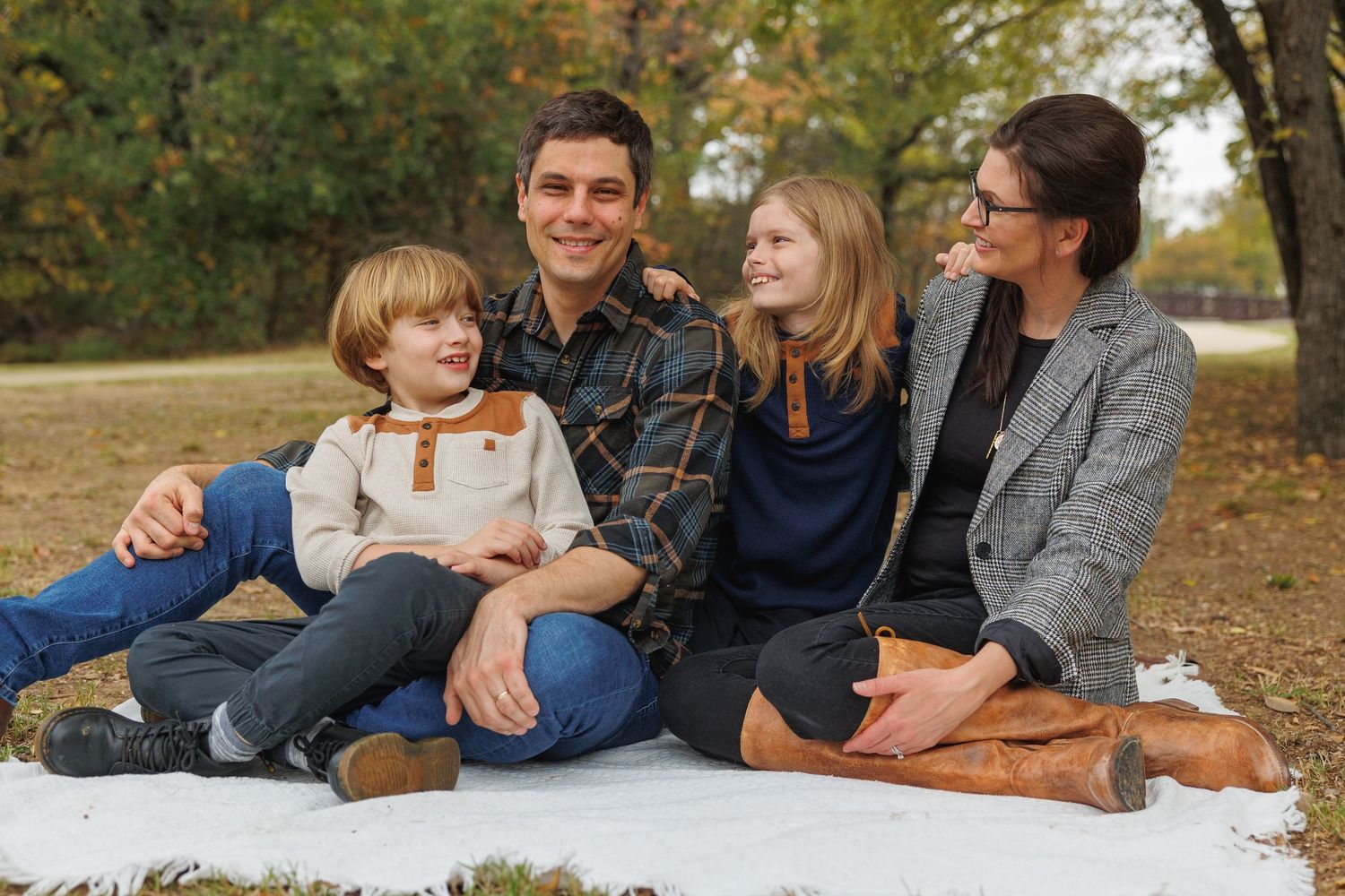 Fall family photo session with people relaxing on blankets outdoors during autumn with colorful leaves around them.
