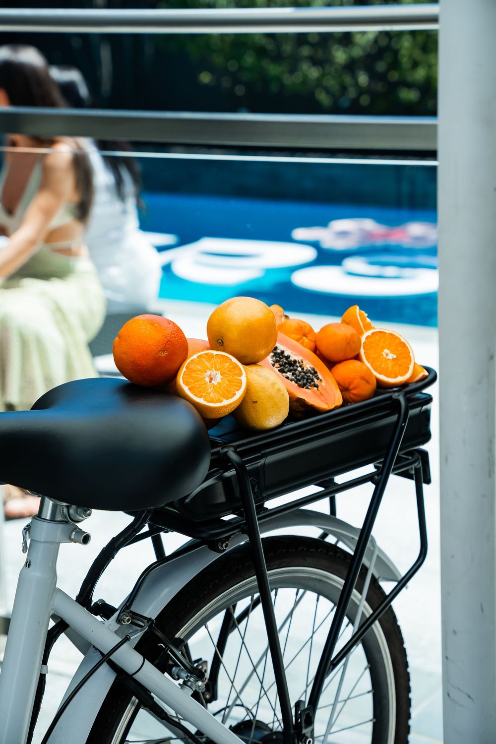 Fresh oranges and tropical fruits arranged on a black bicycle rack against a blue background.