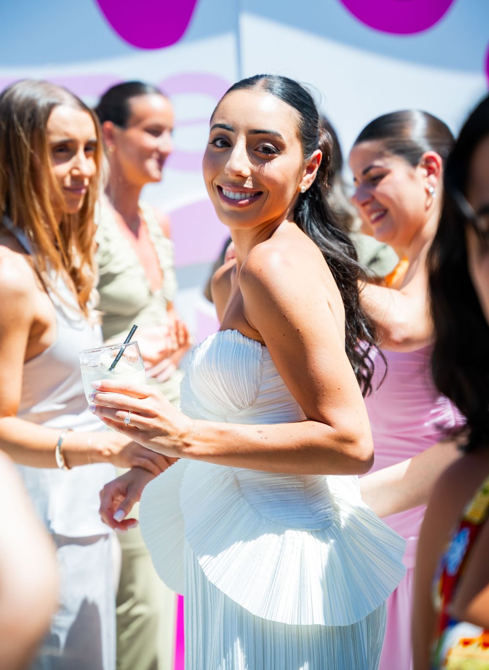 A group of friends laugh and react emotionally in matching pink and white outfits during a special celebration.