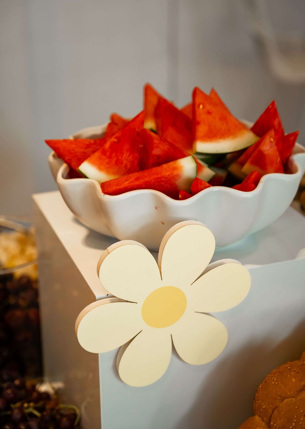 Fresh red watermelon triangles served in a white scalloped bowl with decorative paper flower accent.
