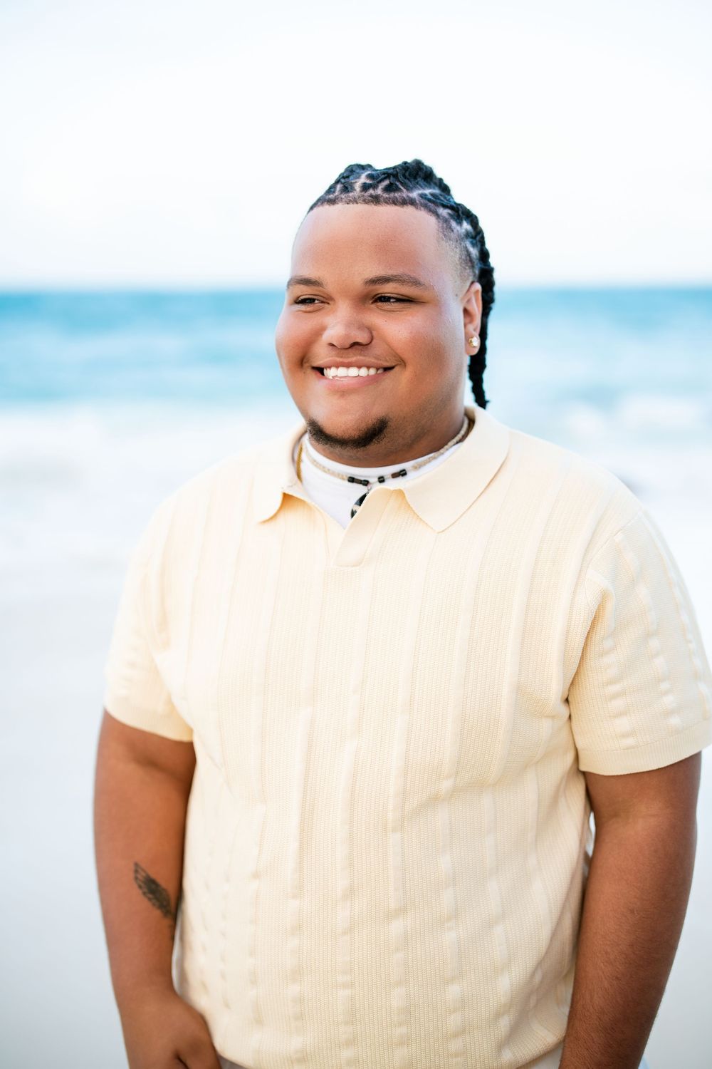 Smiling person in cream-colored polo shirt standing on beach with ocean in background.