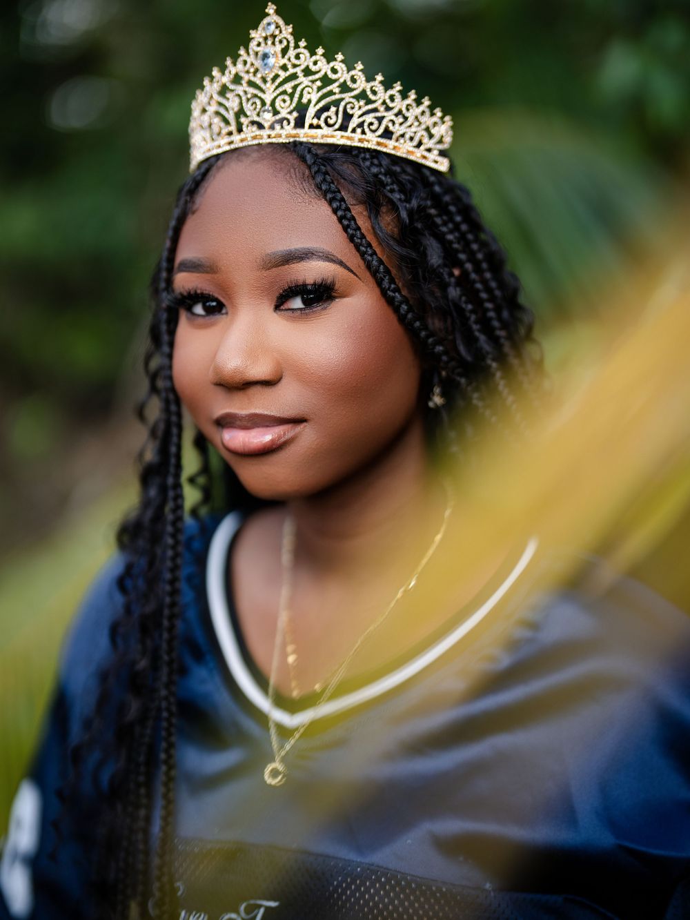 Elegant beauty wearing a delicate golden crown and navy dress with long braided hair against a soft blurred background.