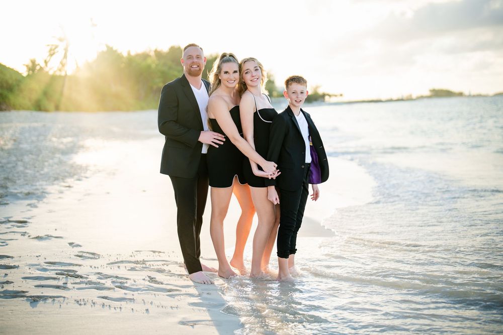 Group standing in shallow water at sunset along a beautiful beach wearing formal attire.