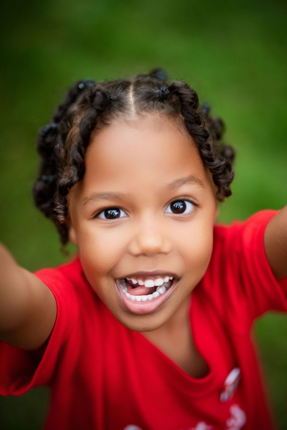 A joyful expression shines through with a bright smile and curly braided hair against a blurred green background.