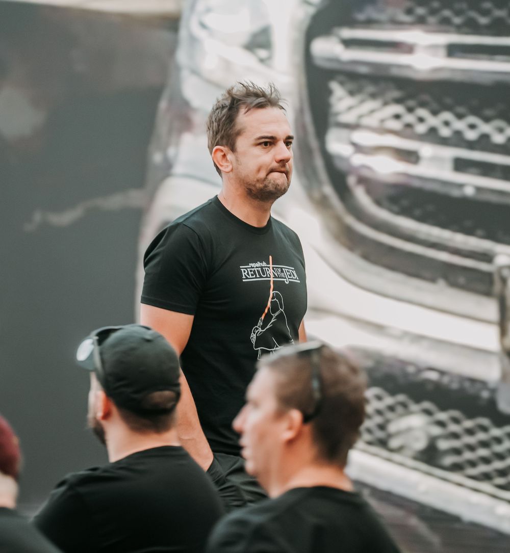 People in black t-shirts gather and interact during what appears to be a backstage or event setting.
