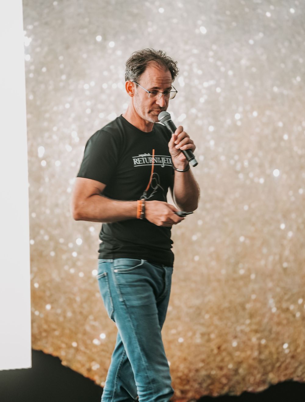 A figure in a black t-shirt performs on stage against a sparkly backdrop in a dynamic sequence of poses.
