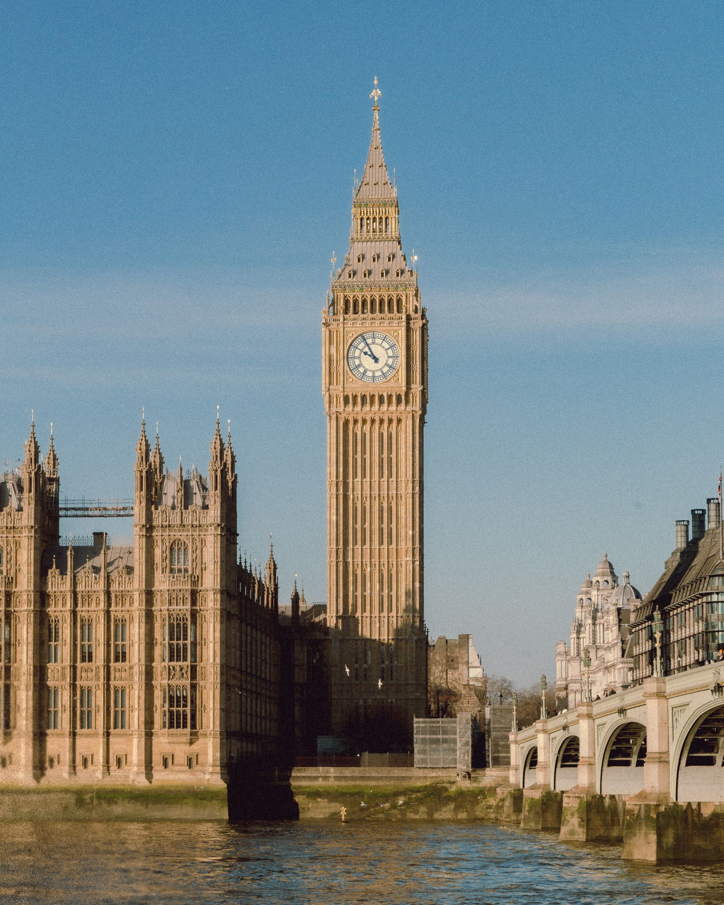 Big Ben tower and Houses of Parliament along the Thames River on a sunny day in London.