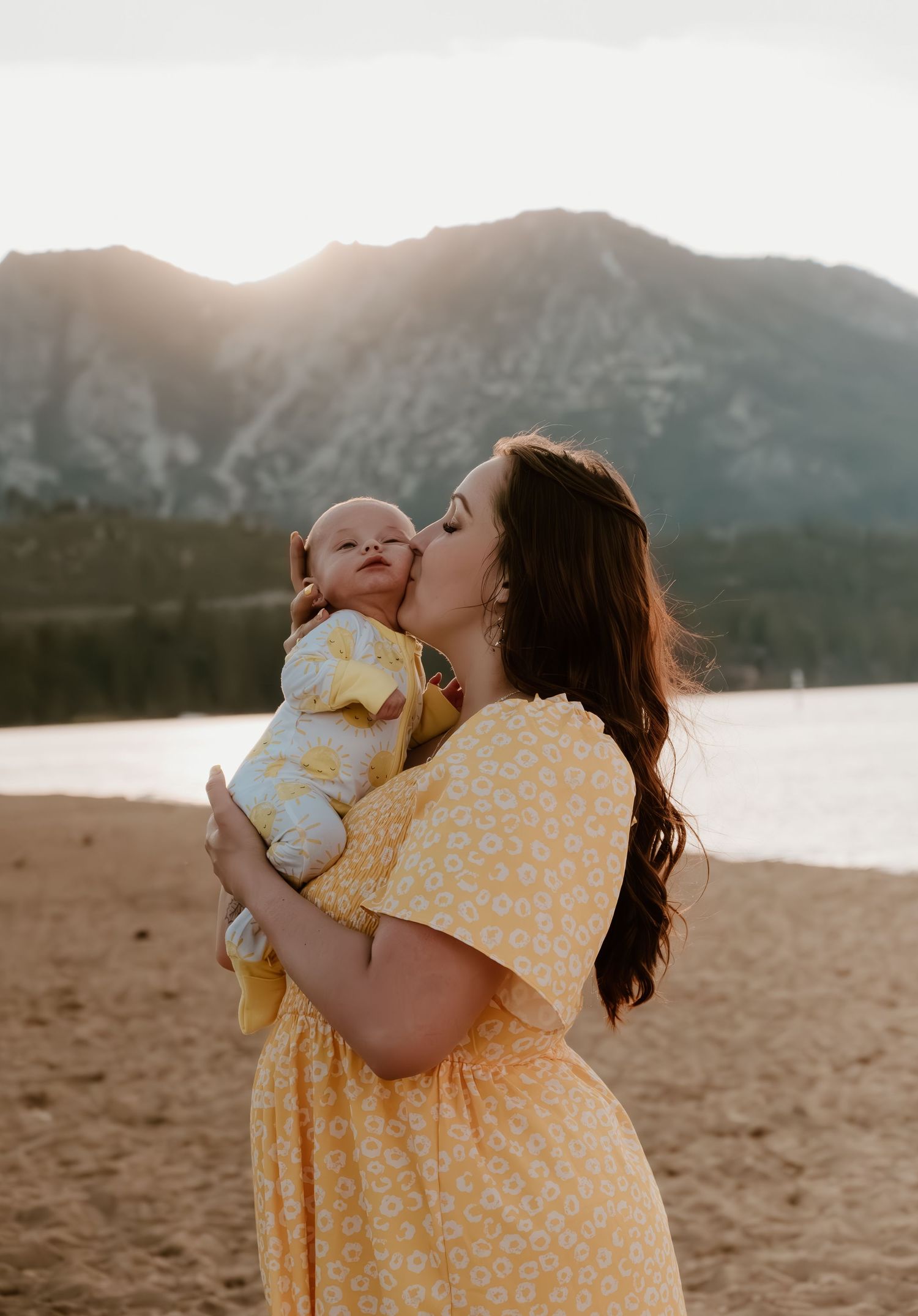 A tender moment captured at sunset by a mountain lake, featuring yellow floral dresses and warm embraces.