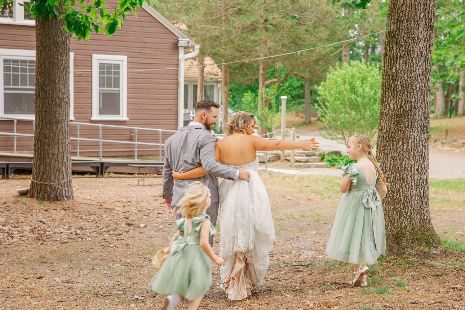 A group walks down a dirt path between trees near a brown cabin in a rustic outdoor setting.