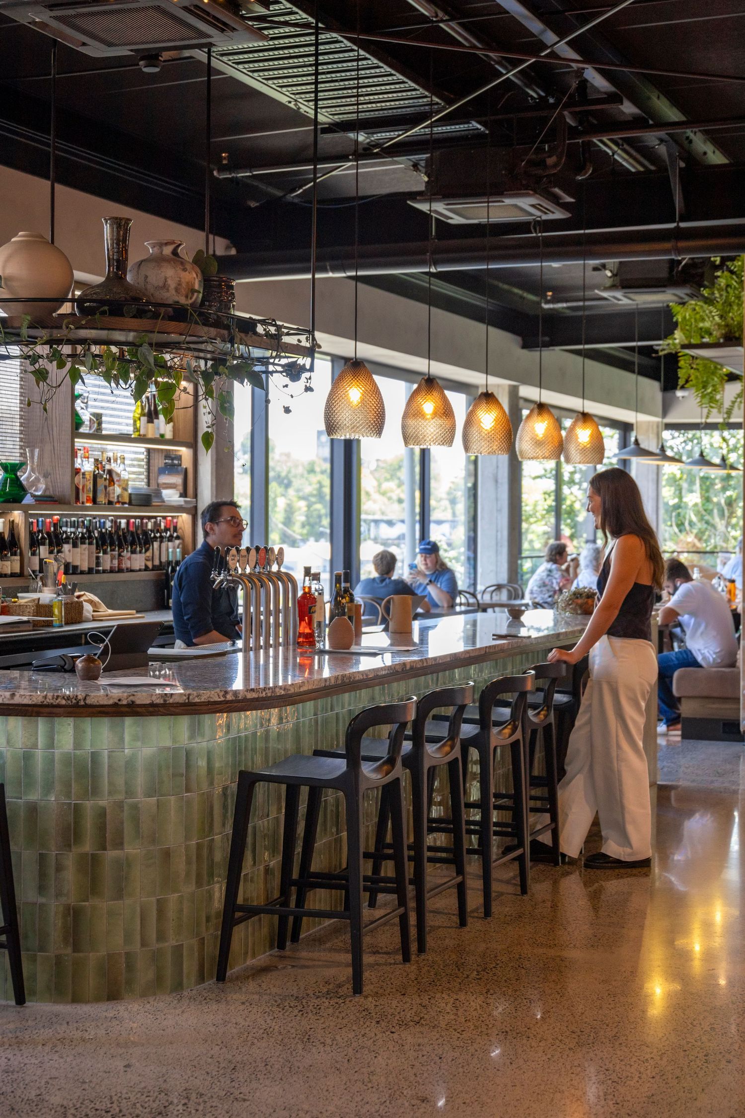 Curved green-tiled bar with hanging lights and patrons seated at stools.