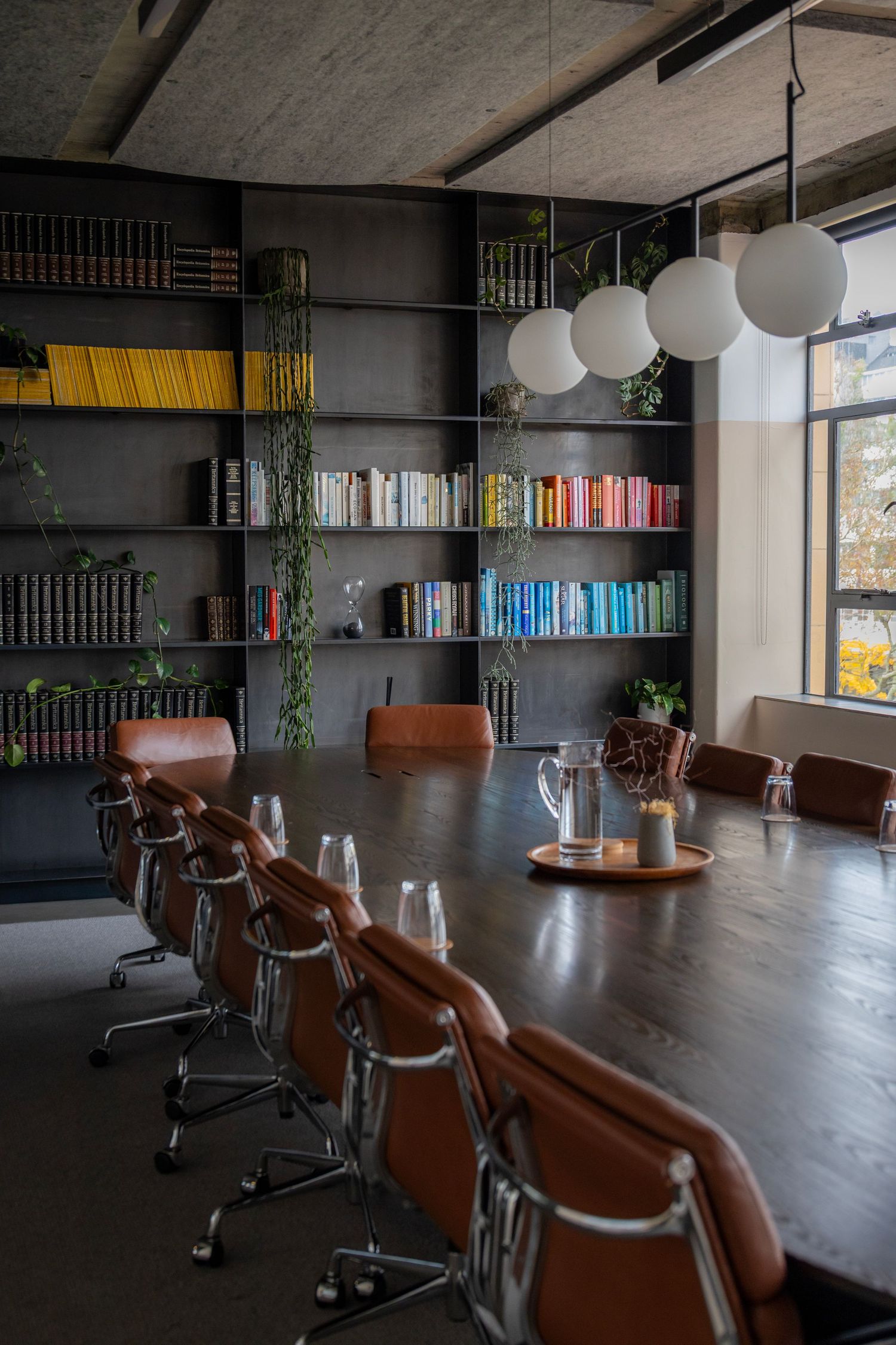 Stylish meeting room with brown leather chairs, dark bookshelves, and globe pendant lights near tall windows.