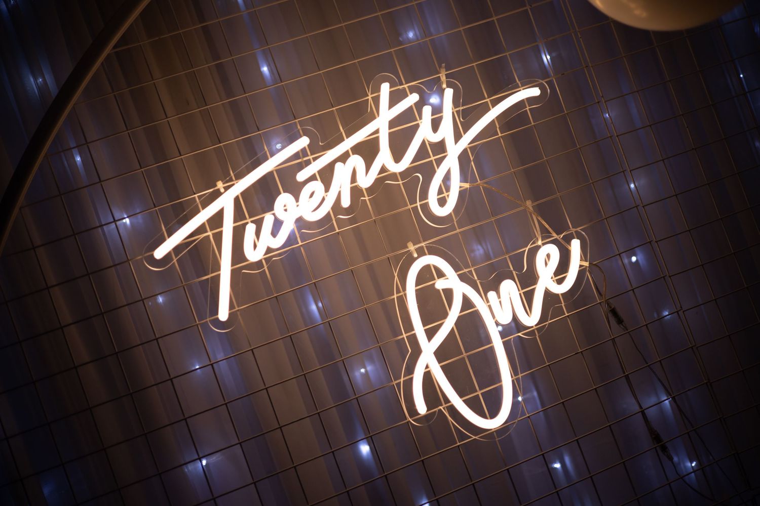 A neon sign displaying the words 'Twenty One' glows against a dark background with twinkling lights.