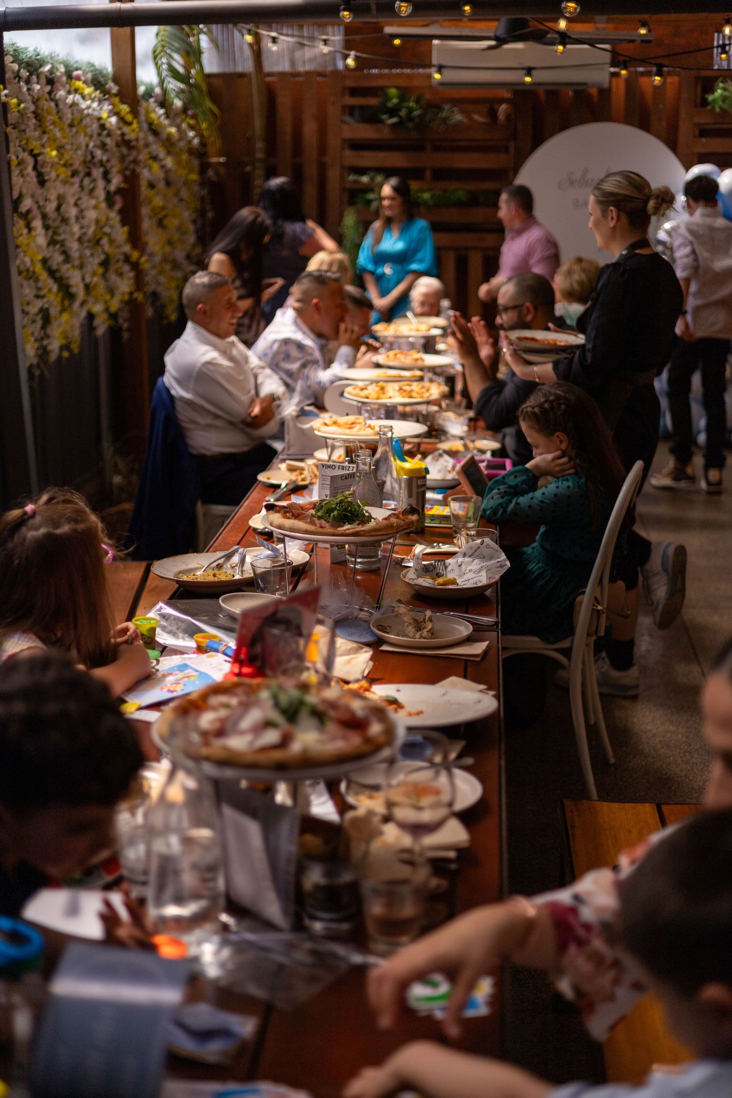 A long table filled with plates and shared dishes in a warmly lit restaurant as guests enjoy a communal dining experience.