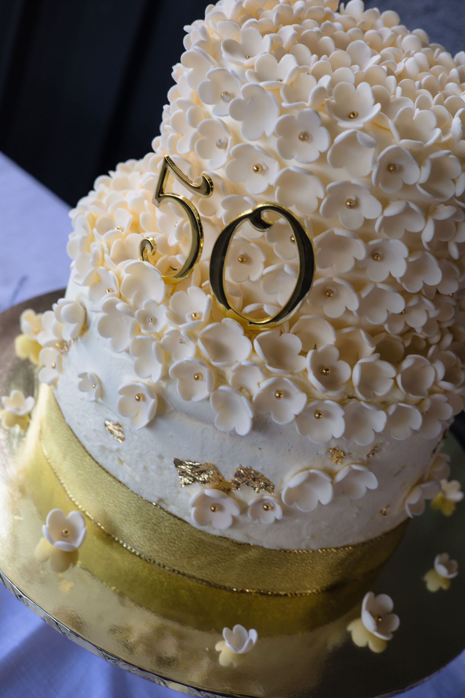 White fondant wedding cake decorated with delicate sugar flowers and gold number 50 topper for anniversary celebration.