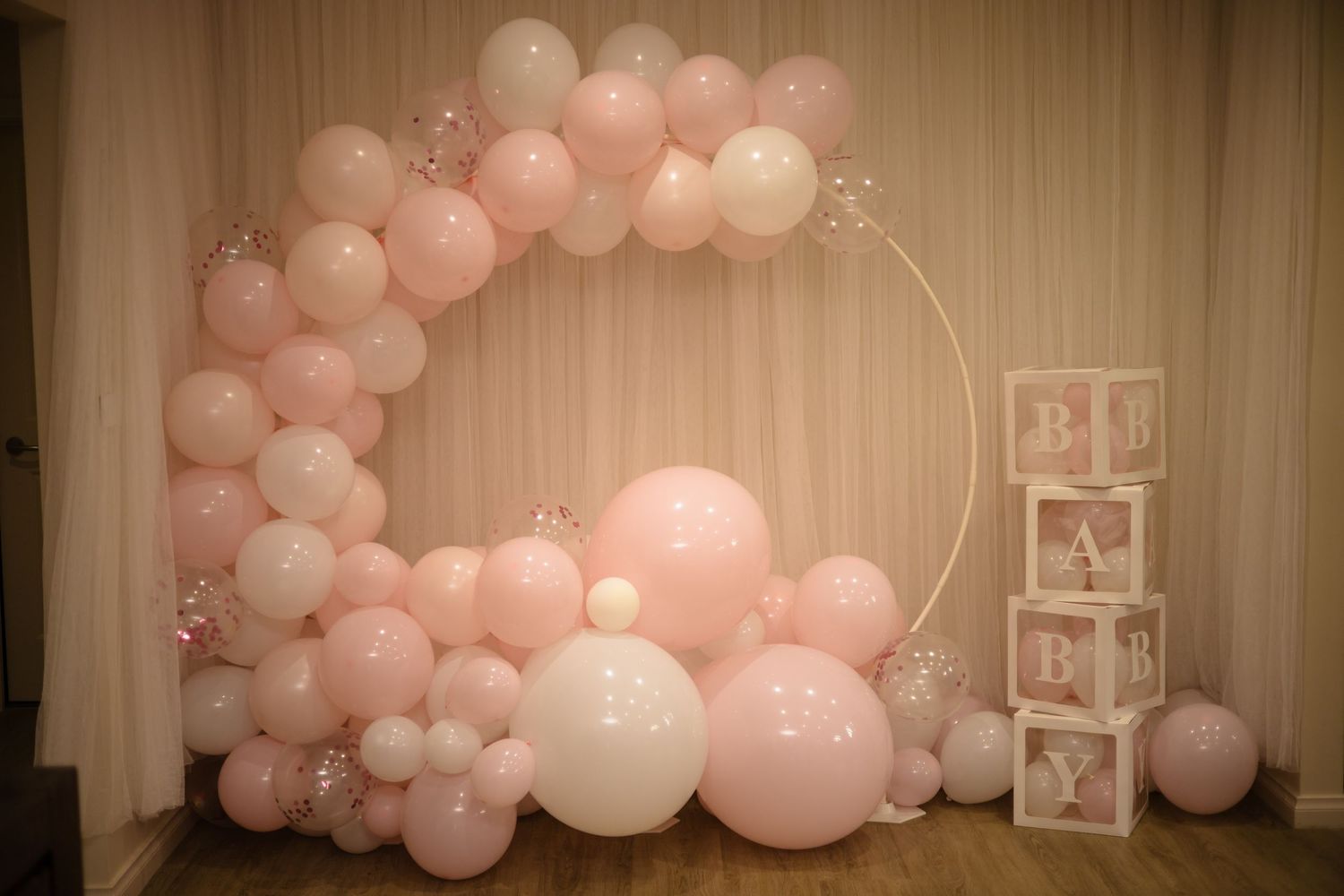 Pink and white balloon arch decoration with decorative boxes for a baby shower or birthday party celebration.