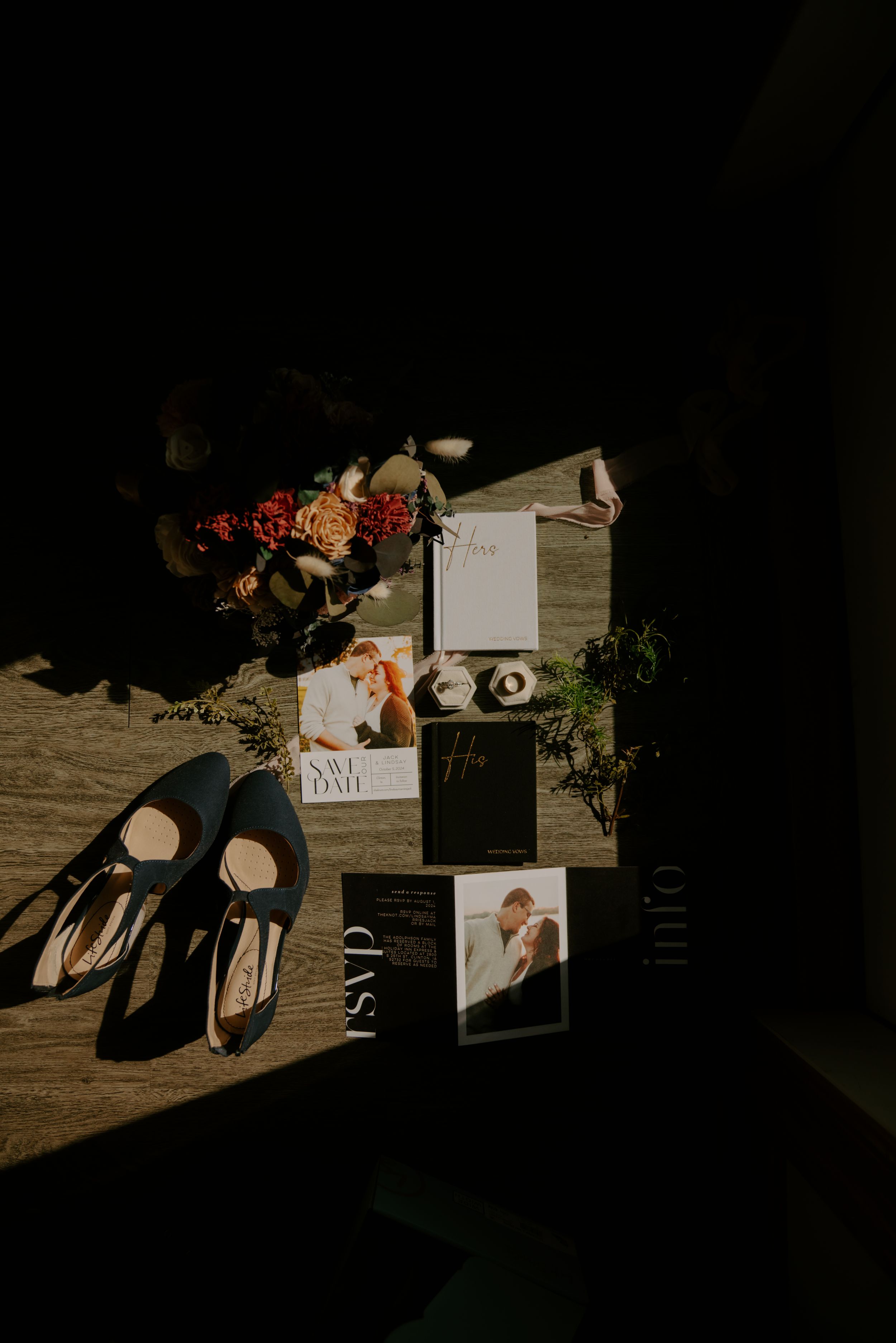 Wedding invitations and paper goods displayed with dramatic shadows on wooden table.