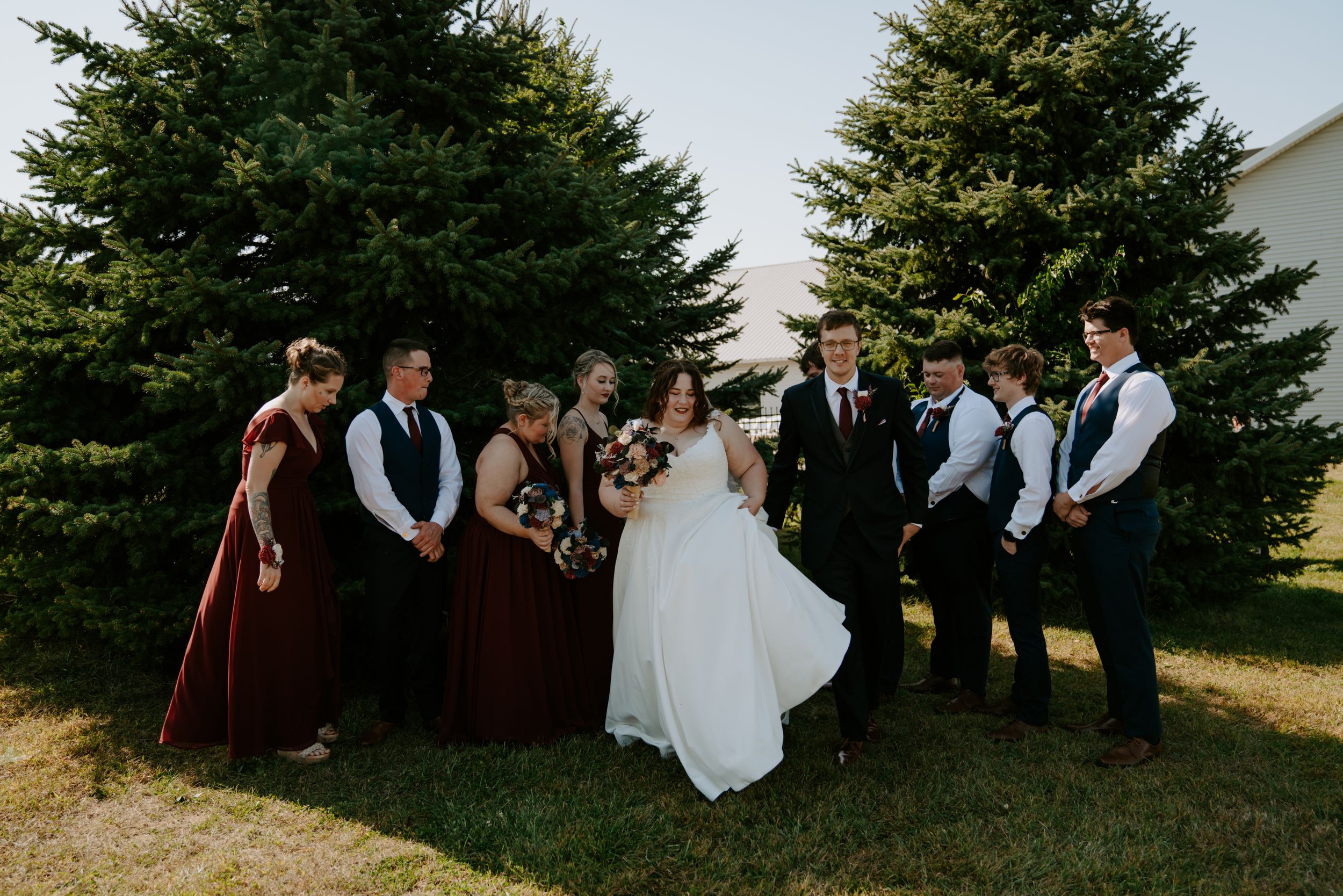 Wedding group photo session taking place in front of tall evergreen trees.