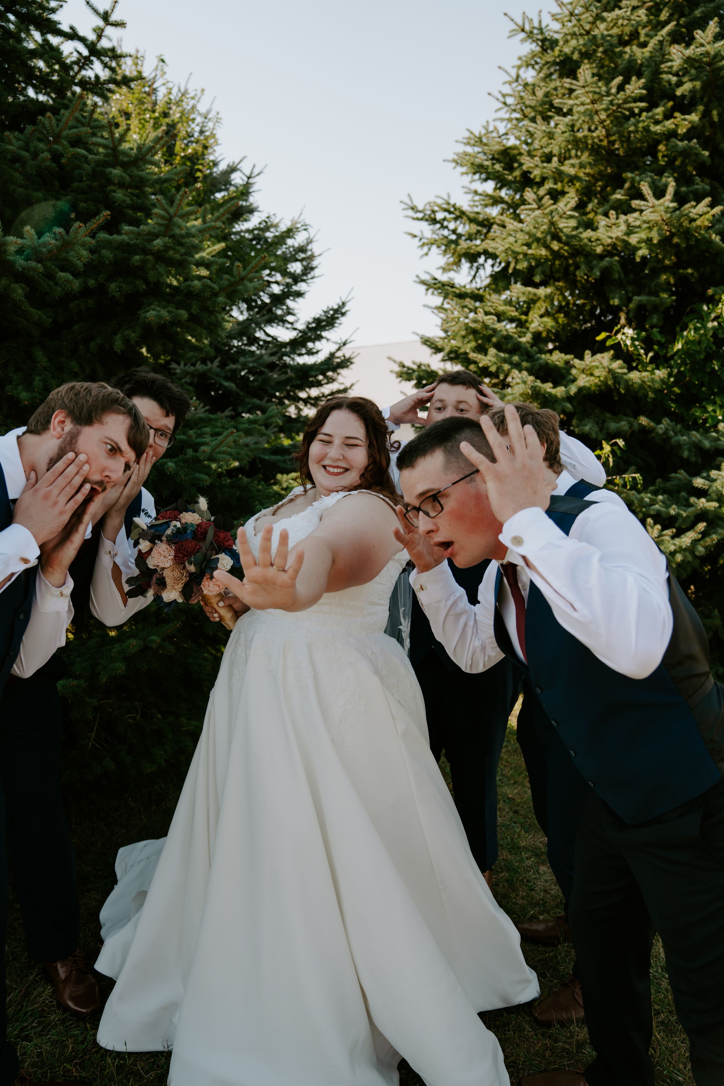 Wedding party members playfully pose together on a sunny afternoon outdoors.