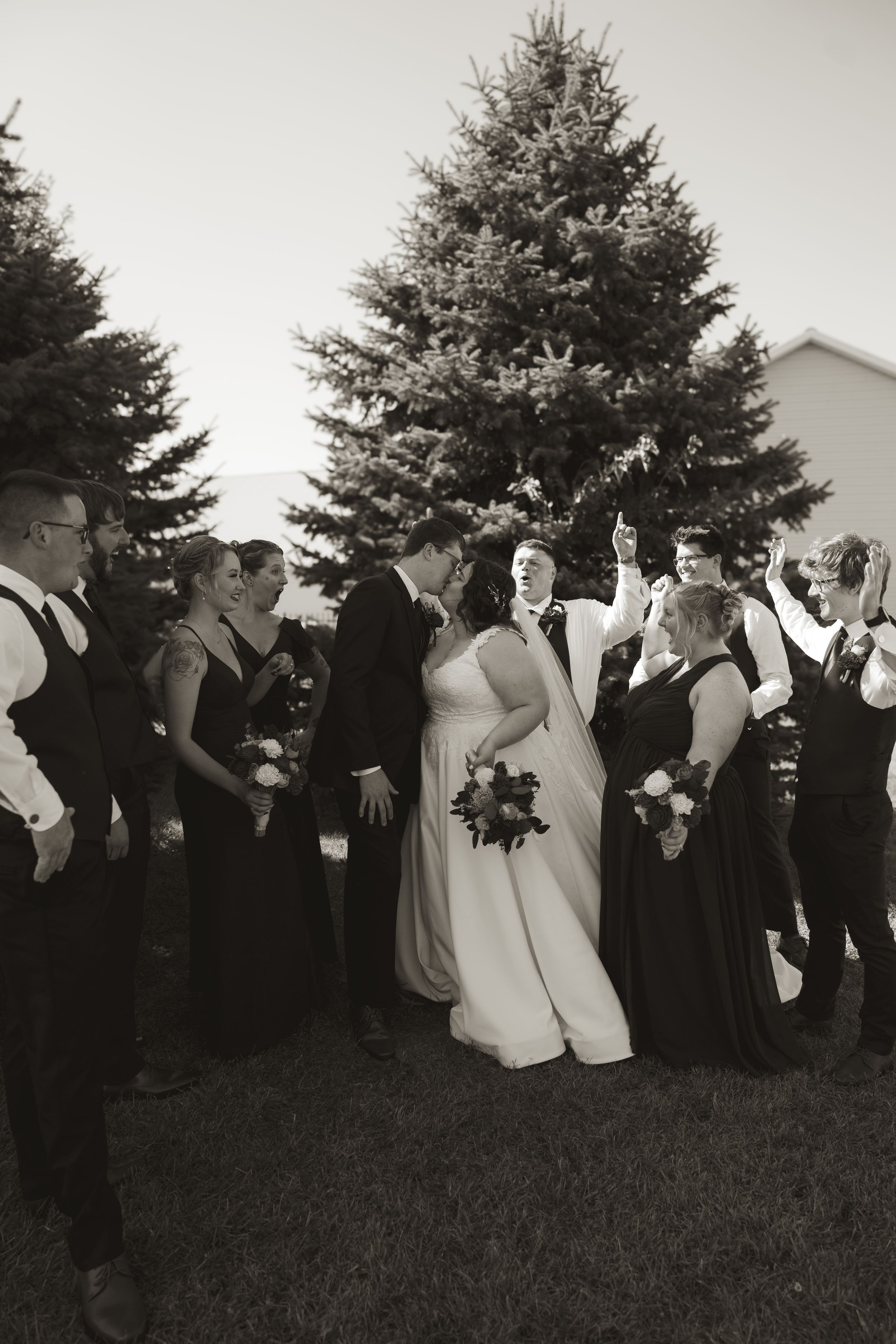 Wedding guests and bridal party gather outdoors in black and white formal attire against a natural backdrop.