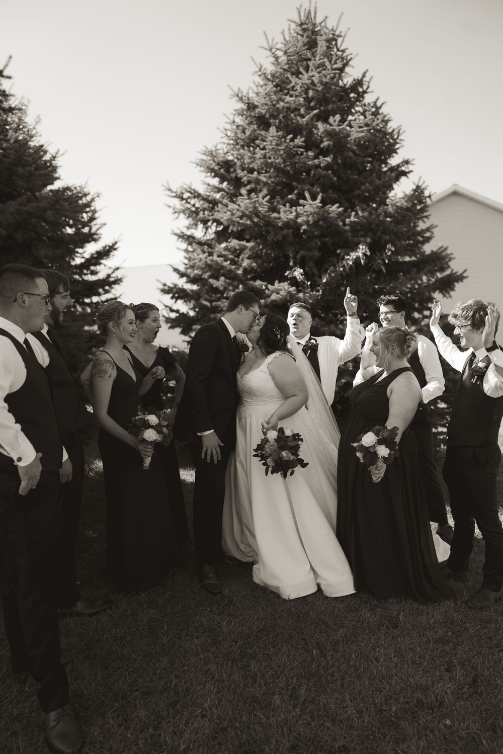Wedding guests and bridal party gather outdoors in black and white formal attire against a natural backdrop.