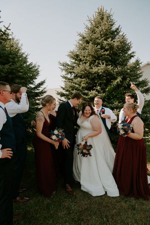 Wedding party in burgundy and white attire poses playfully outdoors during photo session.