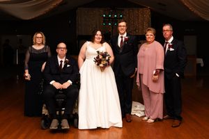 Wedding party members seated in formal attire inside a dimly lit reception venue.