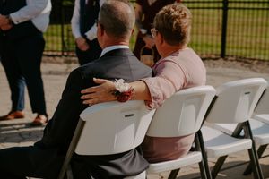 Wedding ceremony guests seated in white chairs outdoors on a sunny day.