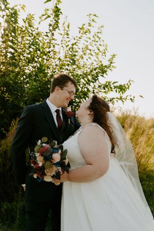 Romantic outdoor wedding portrait with couple embracing against natural foliage backdrop.
